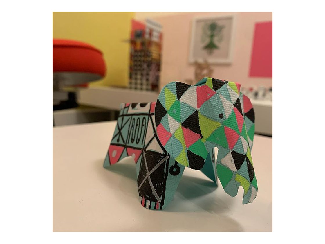 An image of a three dimensional paper elephant decorated with multi-colored triangles that form a geometric pattern.