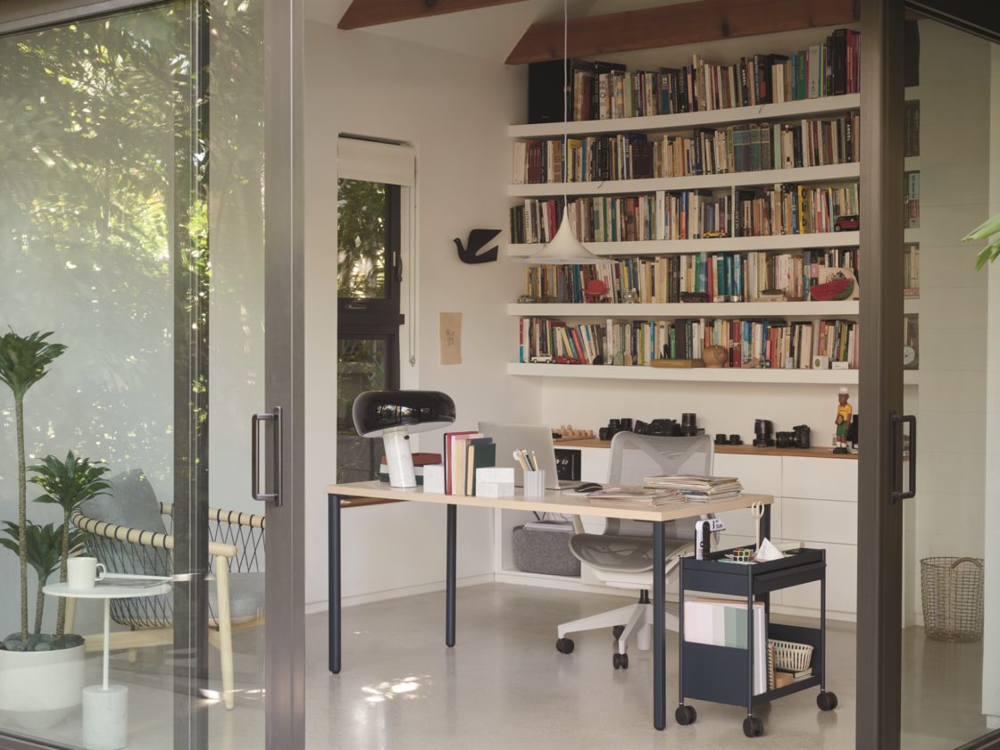 A home office with a navy OE1 Storage Trolley holding personal items in its open top and folders and books in its bottom shelf.