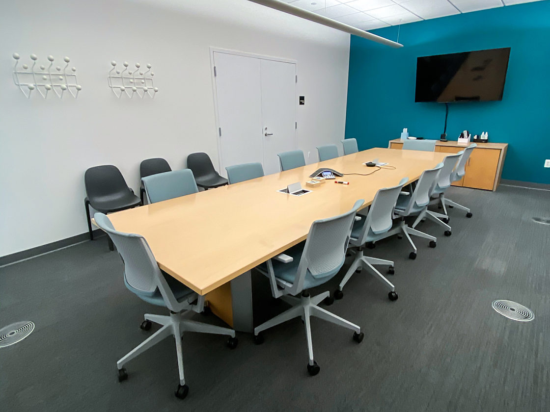 A long wood conference table surrounded by grey task chairs.