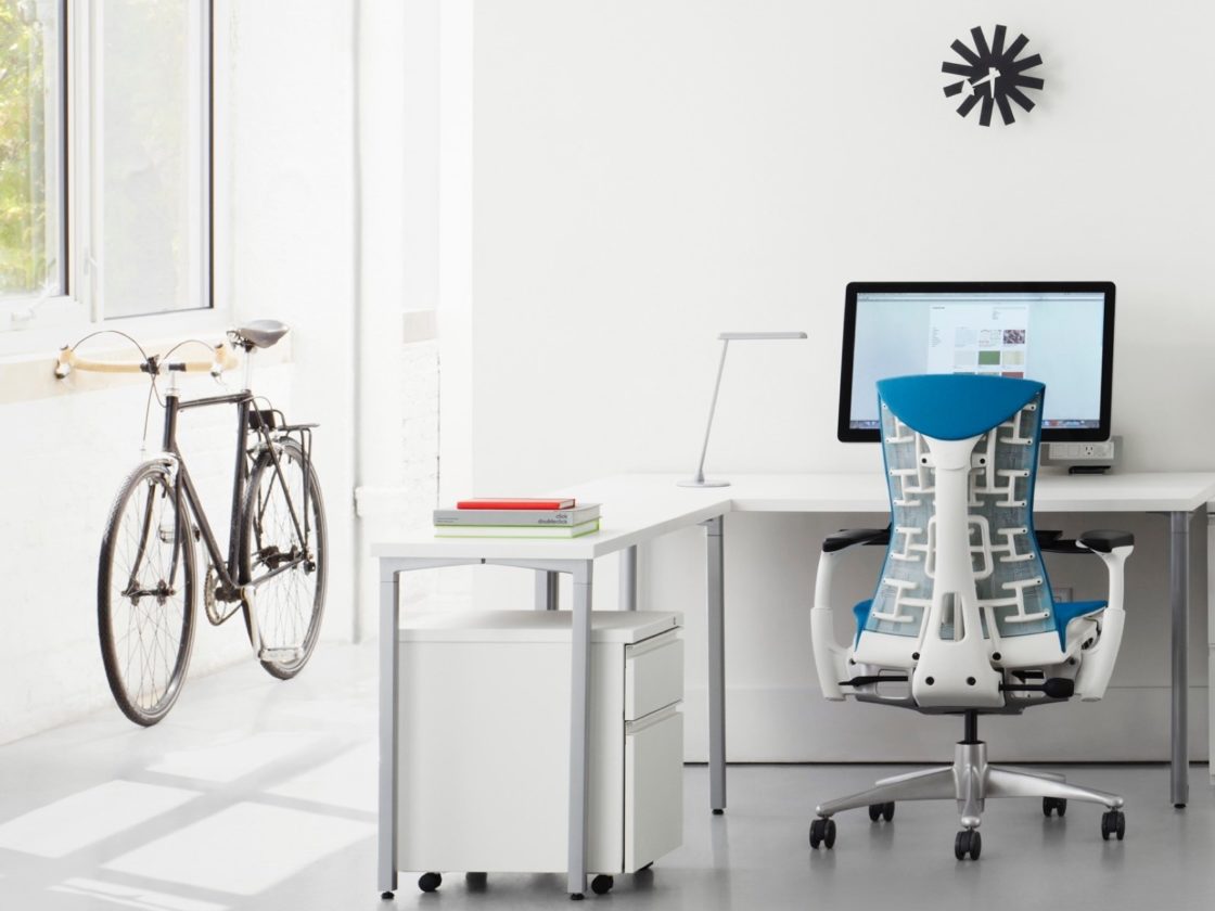 A photo a blue Embody chair in front of a L-shaped white desk with a white pedestal underneath it and a computer on top.