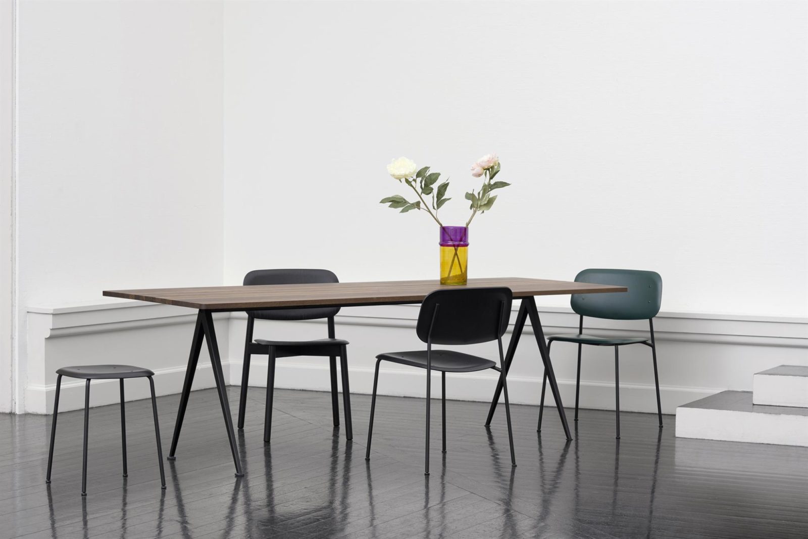 An office with black HAY Soft Edge 10 chairs arranged around a wood Pyramid Table holding a vase of flowers.