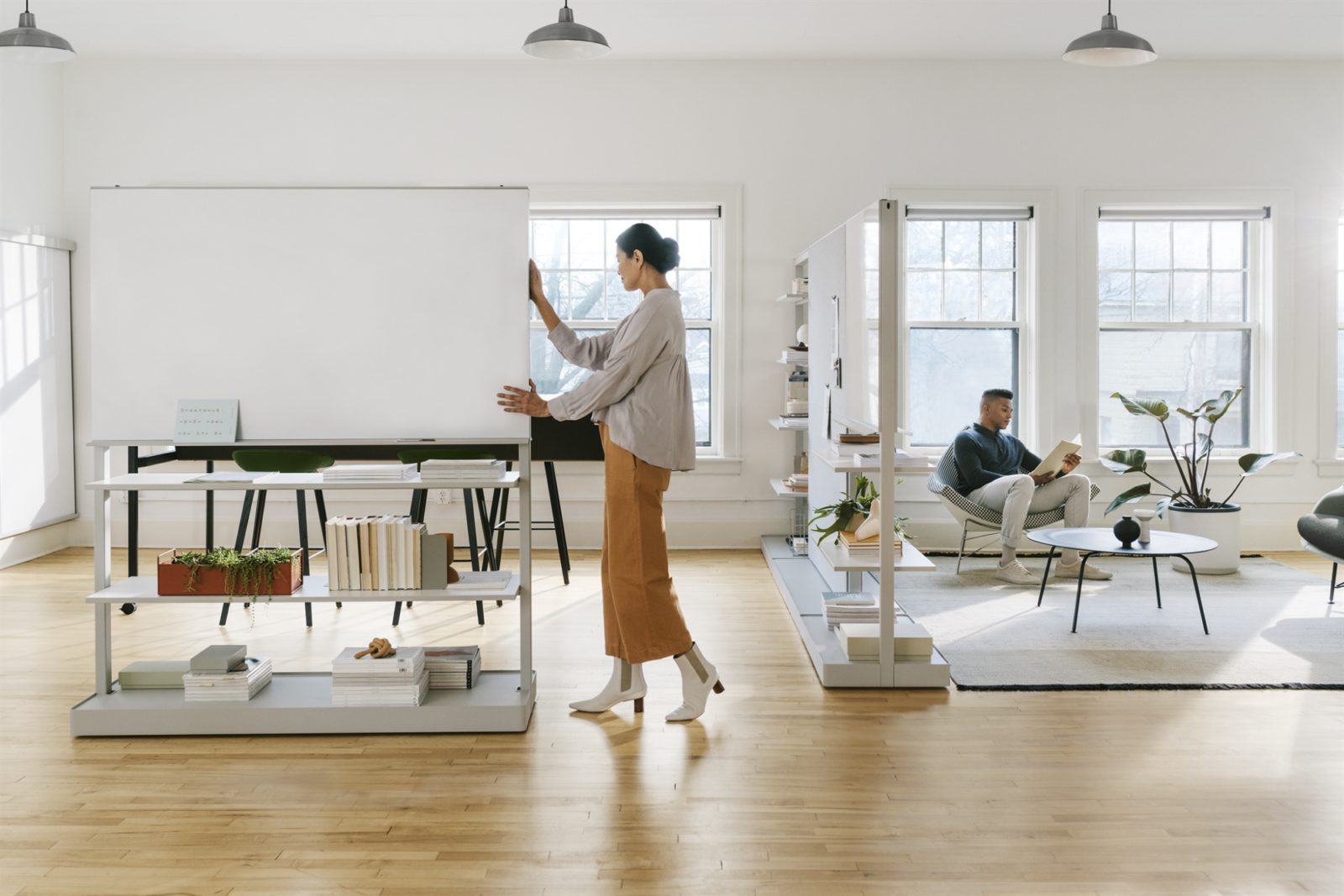 A woman pushes an OE1 Agile Wall with an integrated whiteboard above two storage shelves across the office.