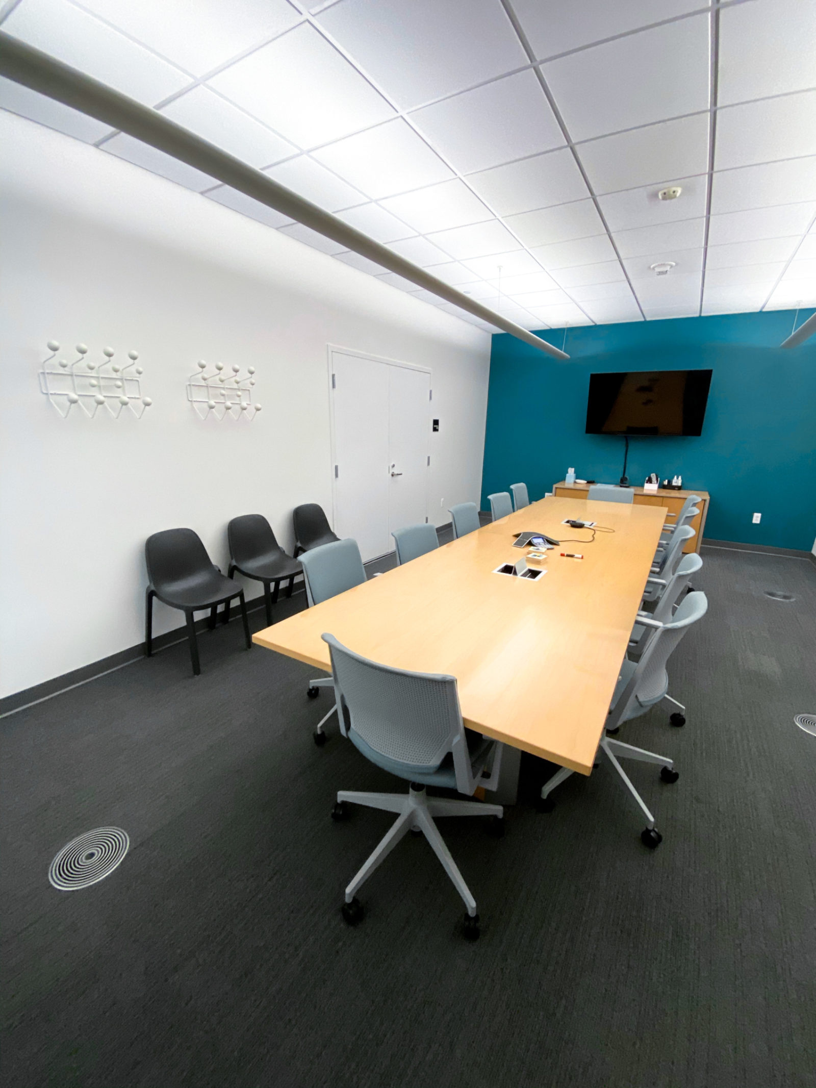 A long wood conference table surrounded by grey task chairs.
