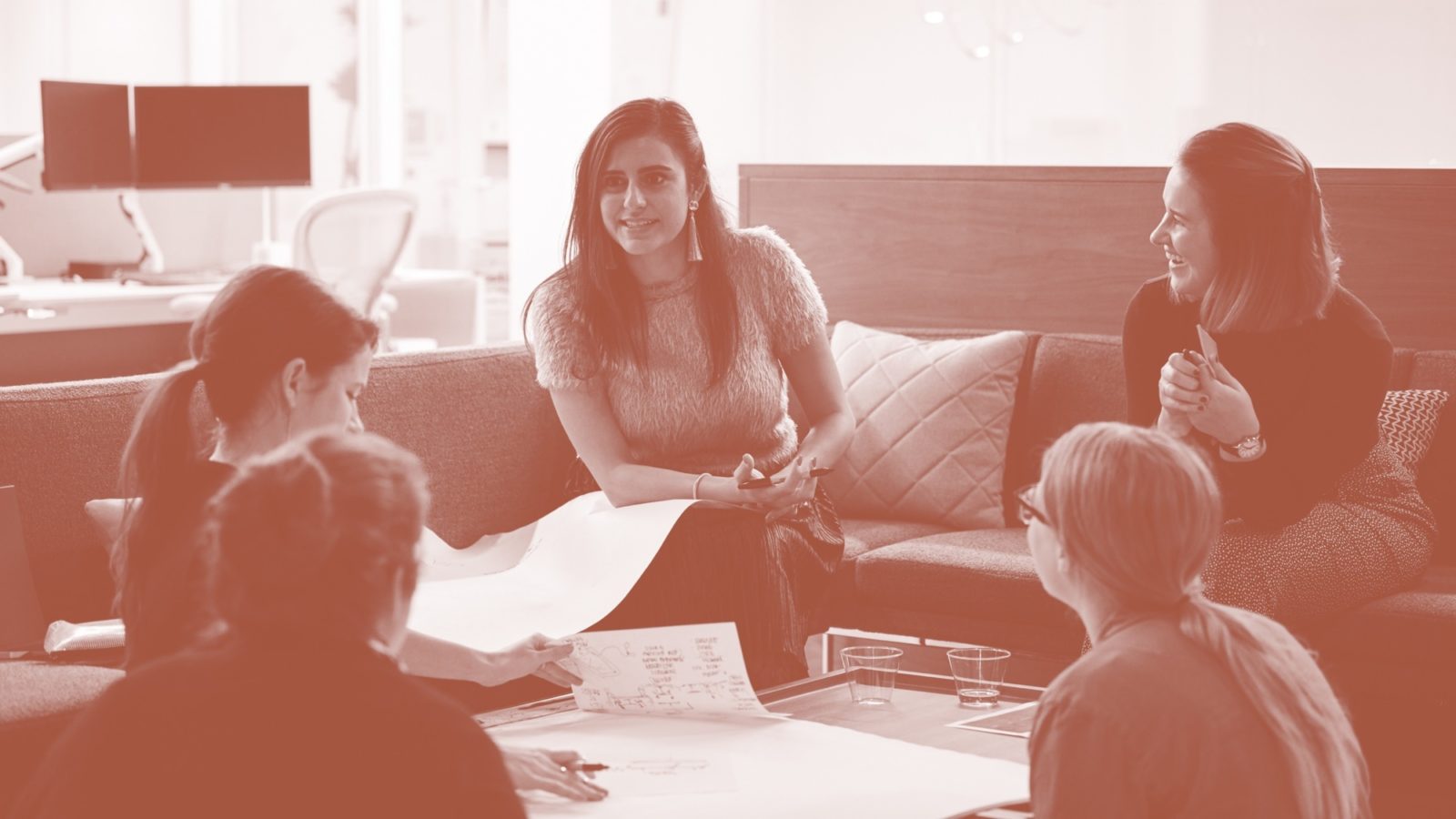 A group of designers seated around the coffee table with some seated on the couch and some on the floor at MarxModa headquarters.