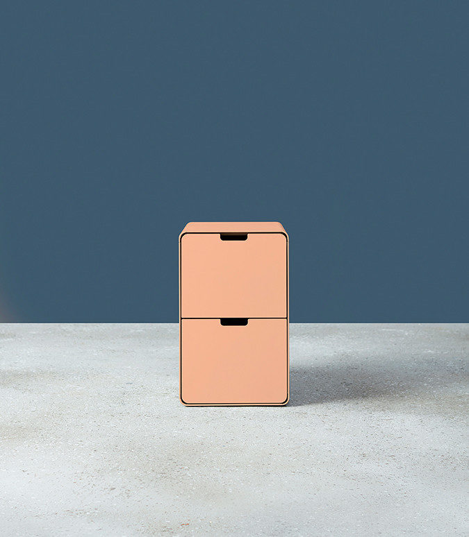 A pink Montisa Russ storage pedestal on a grey floor with a navy background.
