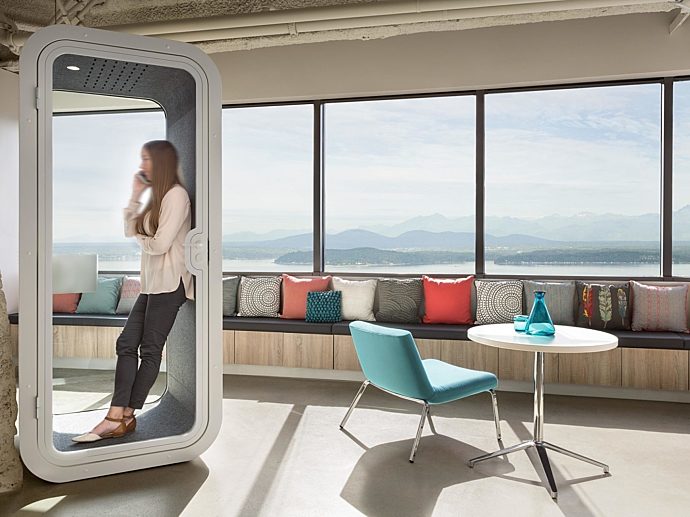 A woman on the phone in a white Framery O in an office next to a lounge chair and side table.