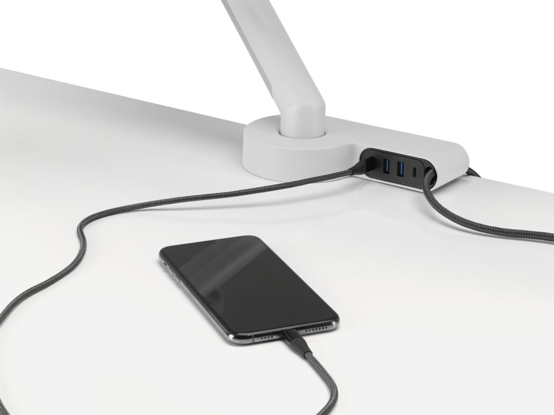 An iPhone sitting on a white worksurface plugged into a white Ondo Connectivity Module to charge.
