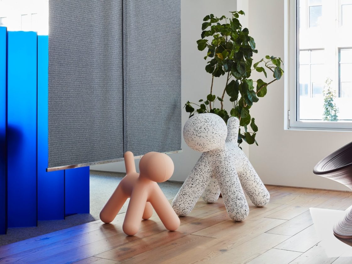 A small pink Magis Puppy next to a large black spotted Magis Puppy in a room with a Magis Spun Chair and a green leafy potted plant.